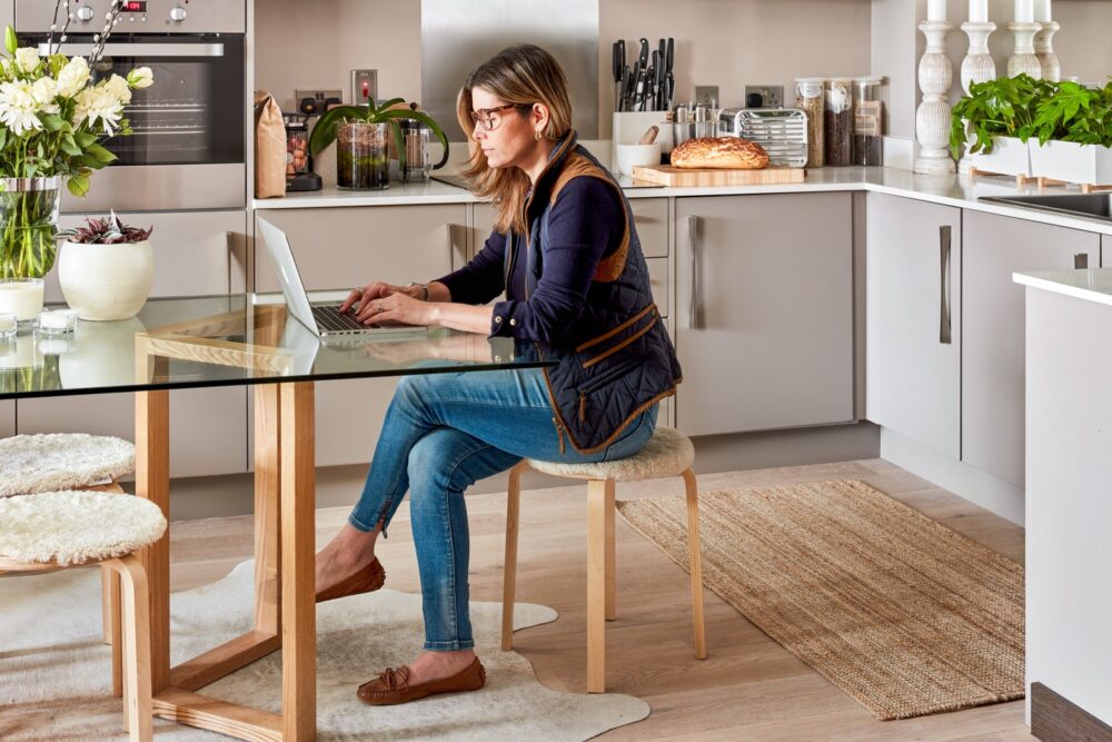 Woman sitting at kitchen table browsing on laptop